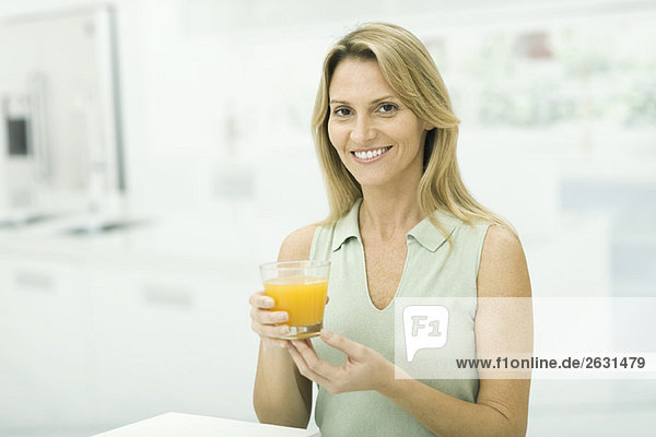 Woman holding up glass of orange juice  smiling at camera  portrait