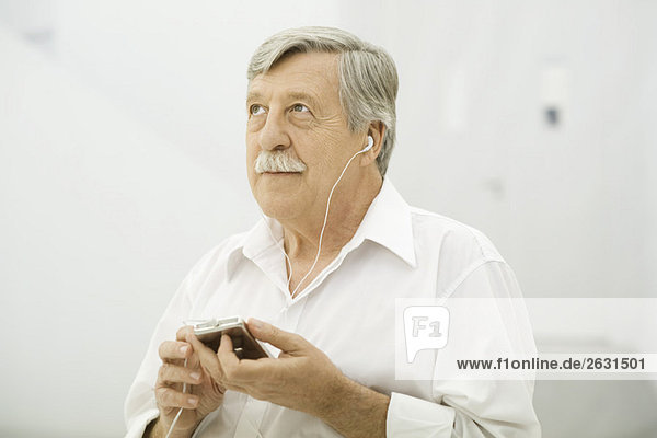 Senior Mann hört MP3-Player  schaut nach oben.