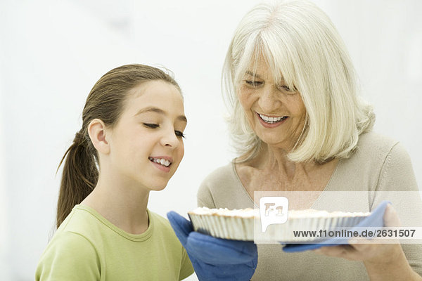 Großmutter und Enkelin schauen auf den frisch gebackenen Kuchen.