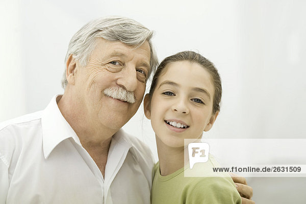 Grandfather and granddaughter leaning close together  smiling at camera  portrait