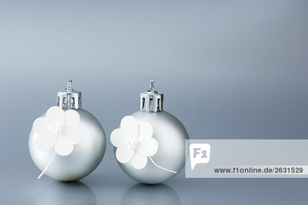 Two silver Christmas tree ornaments decorated with white flowers