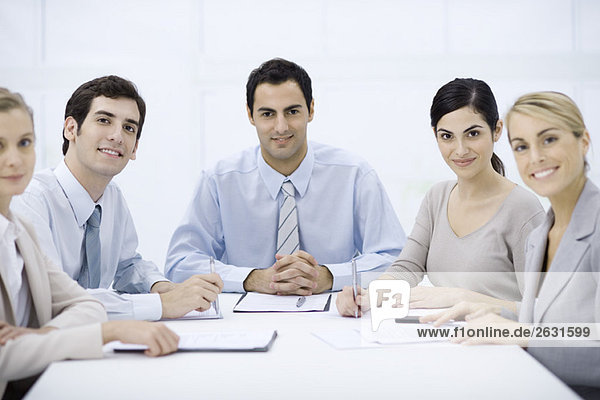 Businessman sitting with colleagues at conference table  smiling at camera