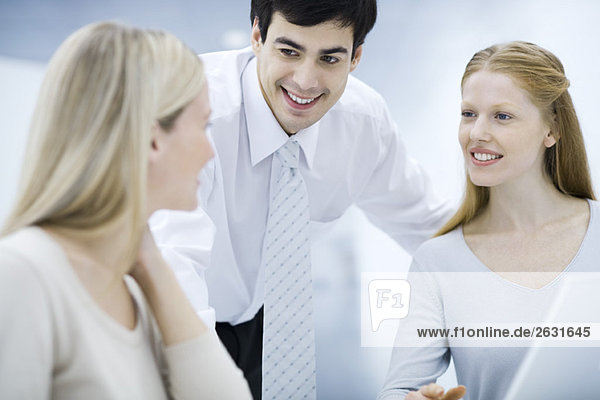 Businessman leaning over  chatting with female colleagues