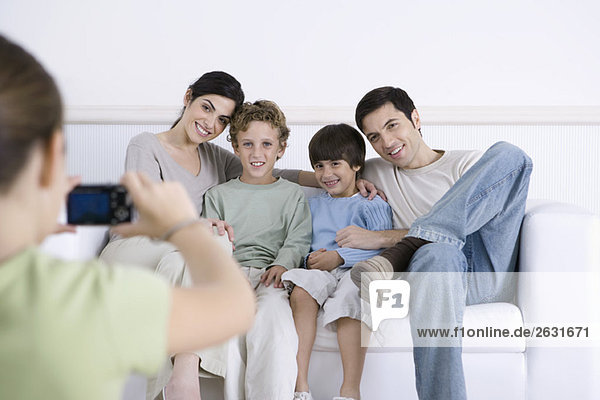 Junges Mädchen fotografiert ihre Eltern und Brüder  die zusammen auf dem Sofa sitzen