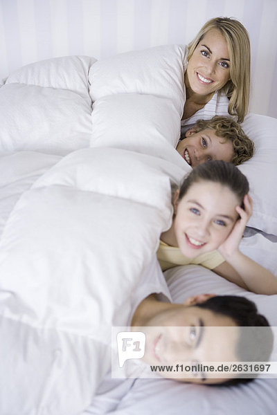 Familie zusammen im Bett liegend  lächelnd vor der Kamera
