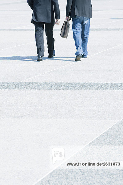Two businessmen walking together wearing business attire  one wearing jeans with blazer