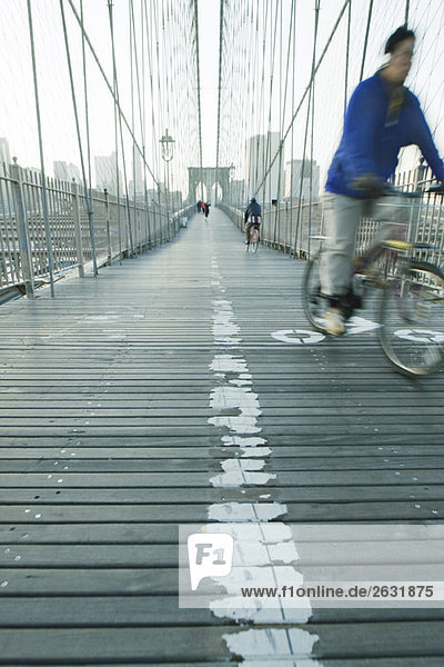 Mann fährt mit dem Fahrrad über den Fußgängerweg der Brooklyn Bridge in New York City  Manhattan Skyline in der Ferne.