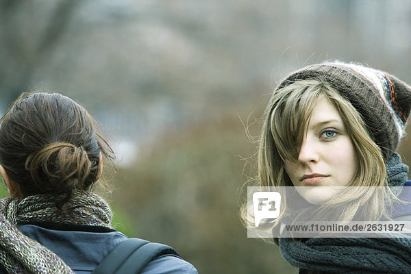Junge Frau geht mit Freundin im Park spazieren  schaut über die Schulter auf die Kamera