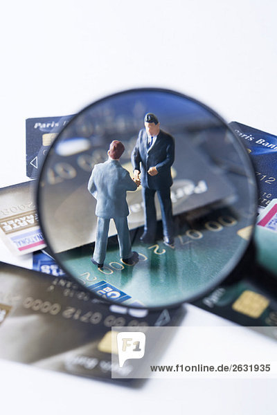 Miniatur-Geschäftsleute schütteln sich die Hände auf einem Stapel von Kreditkarten  durch die Lupe betrachtet.
