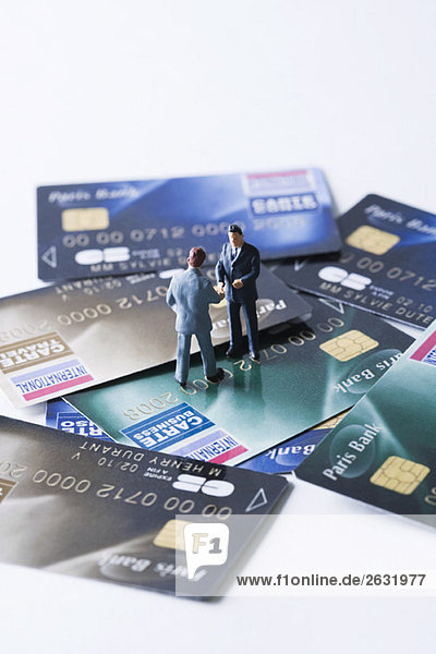 Miniatur-Geschäftsleute schütteln sich die Hände auf einem Stapel von Kreditkarten