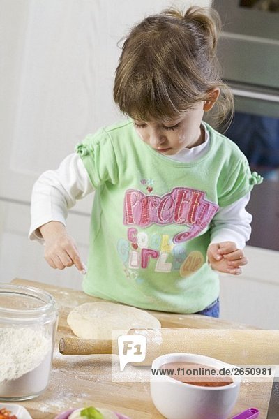 Kleines Mädchen bestäubt Pizzateig mit Mehl
