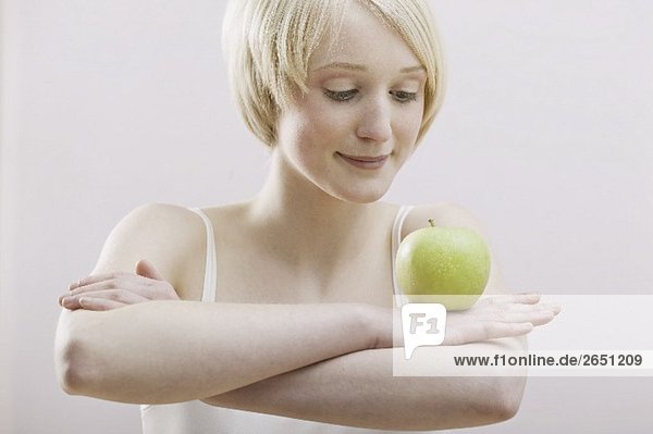 Junge Frau balanciert Apfel auf verschränkten Armen