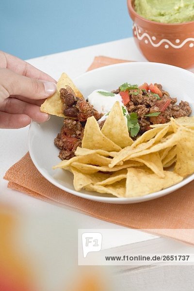 Hand dipping tortilla chip in mince sauce