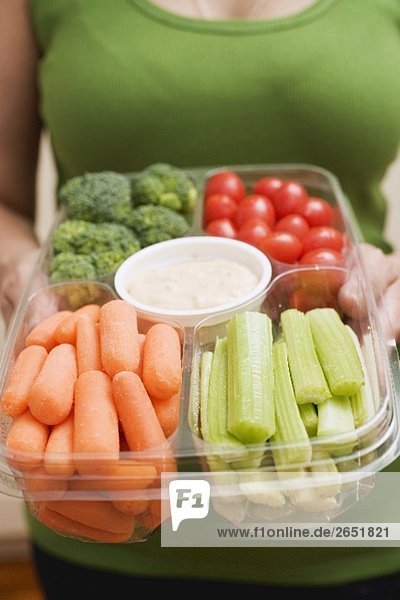 Frau hält Plastikschale mit Gemüse und Dip