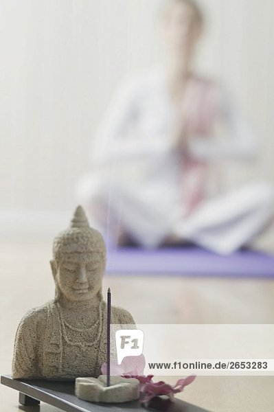 Buddhastatue und Räucherstäbchen  dahinter Frau im Yogasitz