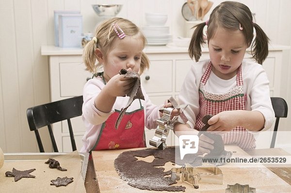 Zwei kleine Mädchen stechen Schokoladenplätzchen aus
