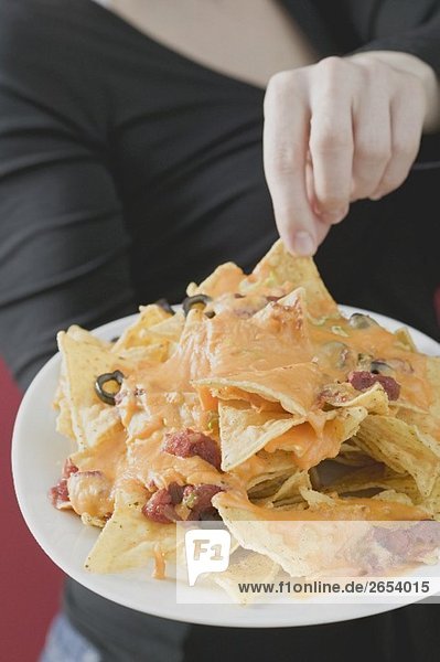 Woman reaching for nachos with melted cheese on plate