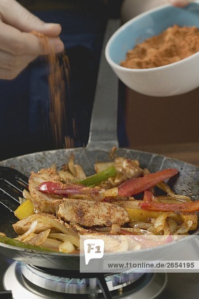Adding chilli powder to chicken with onions and peppers