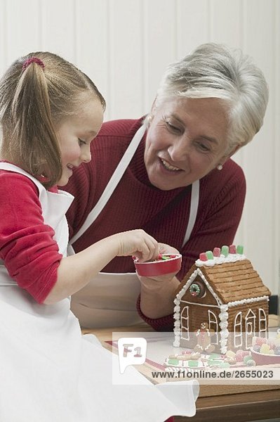 Small girl with grandmother decorating gingerbread house
