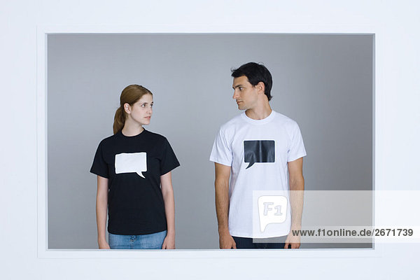 Junger Mann und junge Frau in T-Shirts  die mit leeren Wortblasen bedruckt sind und sich gegenseitig anschauen.