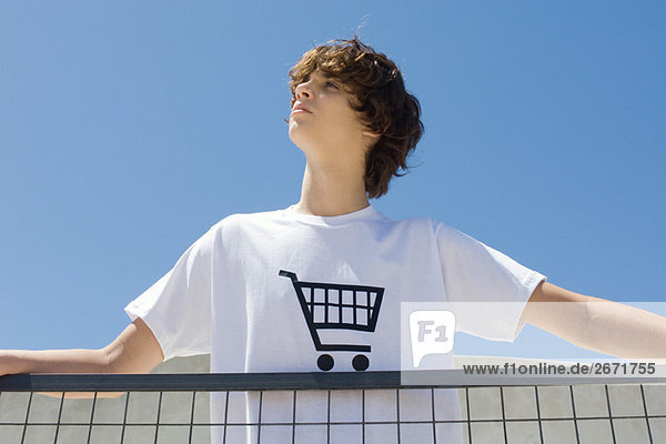 Teenager Junge im T-Shirt bedruckt mit Einkaufswagen  am Geländer stehend  aufblickend