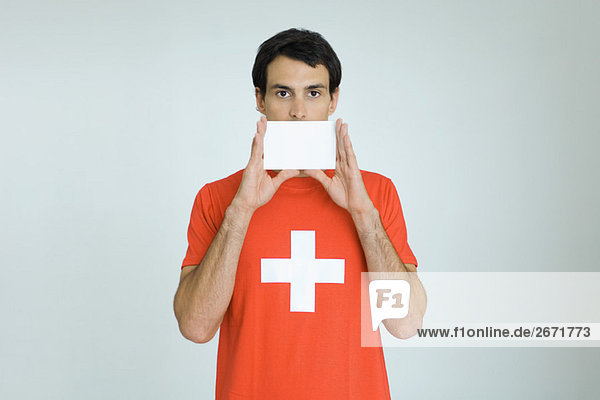 Mann im T-Shirt mit Schweizer Fahne  hält eine leere Karte vor den Mund