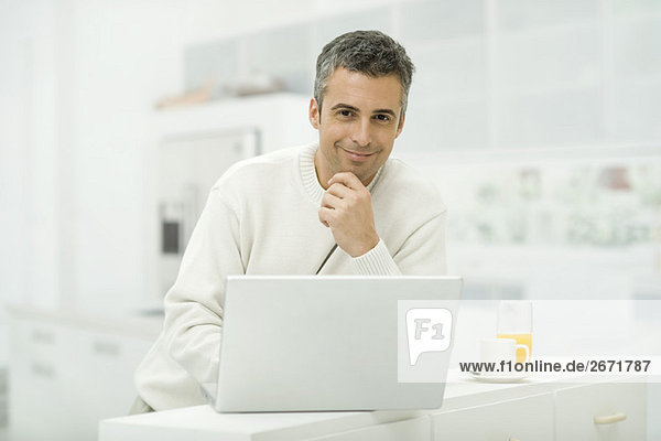 Man using laptop computer in kitchen  smiling at camera