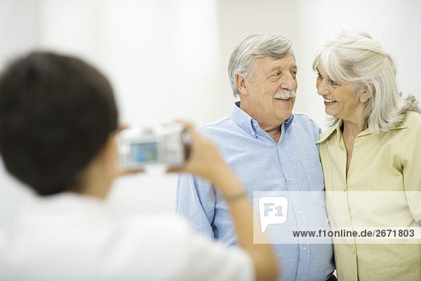 Seniorenpaar wird vom Enkel fotografiert und lächelt sich an.