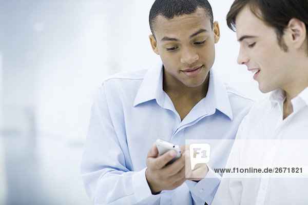 Two young businessmen looking down at cell phone