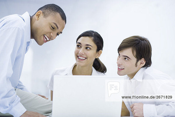 Young professionals sitting around laptop computer  leaning close together  smiling