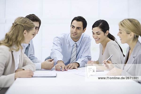 Group of professionals sitting at table  listening to male colleague pointing at document