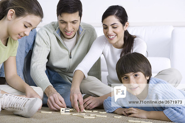 Familie sitzt auf dem Boden und spielt zusammen Domino  Junge lächelt in die Kamera.
