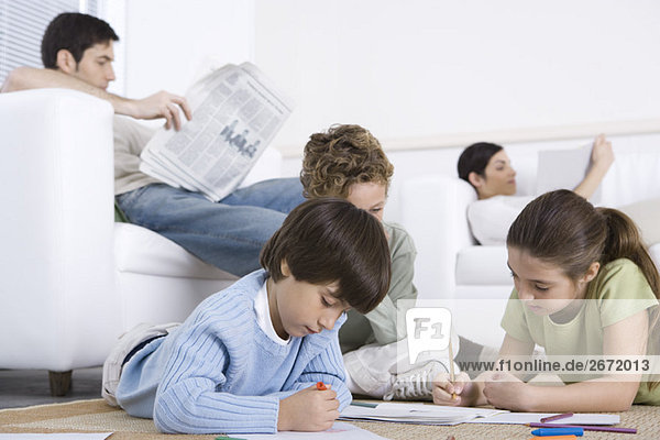 Kinder malen auf dem Boden im Wohnzimmer  Eltern lesen im Hintergrund