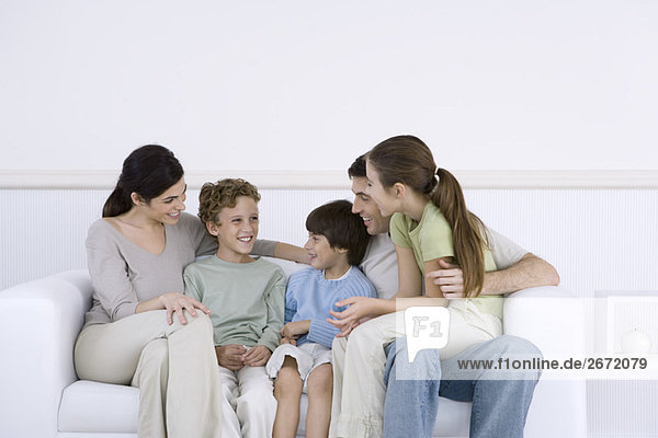 Familie mit drei Kindern  die zusammen auf dem Sofa sitzen und reden.