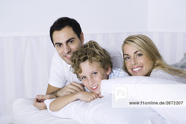 Parents and son lying on bed  smiling at camera  portrait
