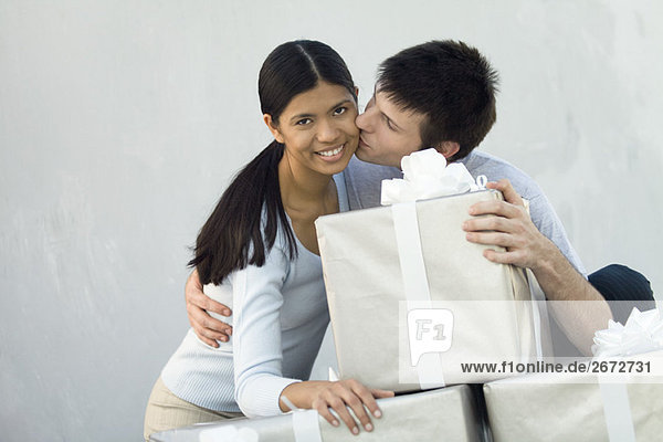 Couple standing behind stack of large gift boxes  man kissing woman on cheek