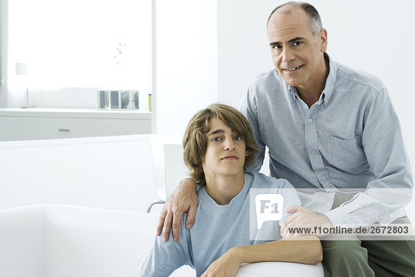 Father and teen son sitting together on sofa  looking at camera  portrait