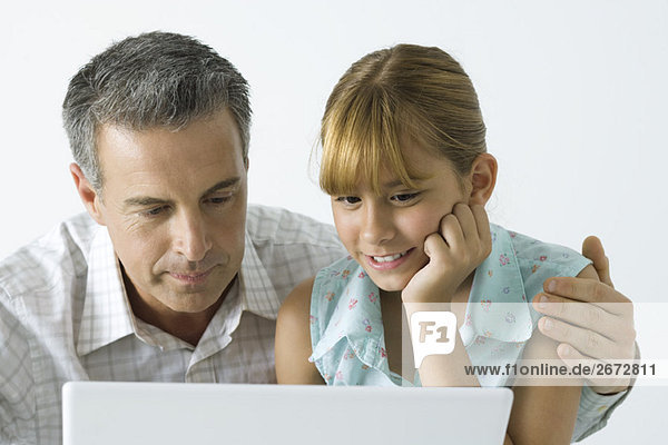 Vater und Tochter schauen zusammen auf den Laptop  der Arm des Mannes um die Schulter des Mädchens.