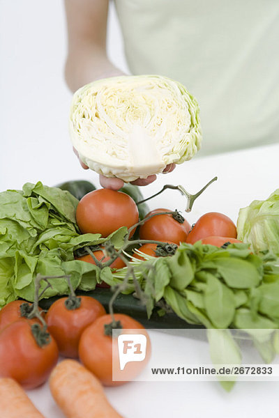 Hand hält halben Salatkopf  im Vordergrund sortiertes frisches Gemüse