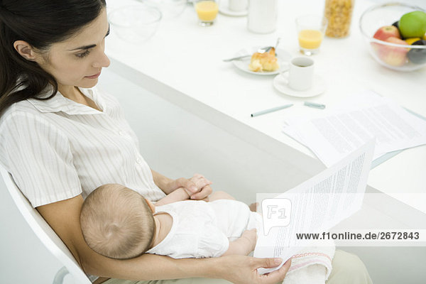 Professional woman sitting at breakfast table  holding toddler  reading document