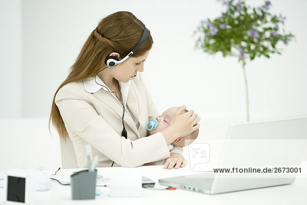 Geschäftsfrau im Büro  hält schlafendes Baby  mit Headset
