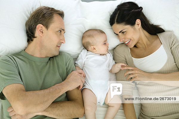 Family resting on bed  baby lying in between parents  overhead view