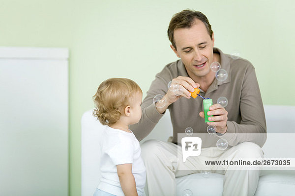 Father and toddler blowing bubbles together