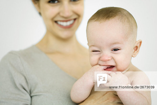 Mutter hält Kleinkind  Baby steckt Hand in den Mund  schaut in die Kamera