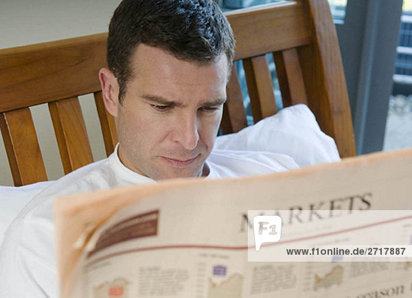 Mann liest Finanzzeitung im Bett