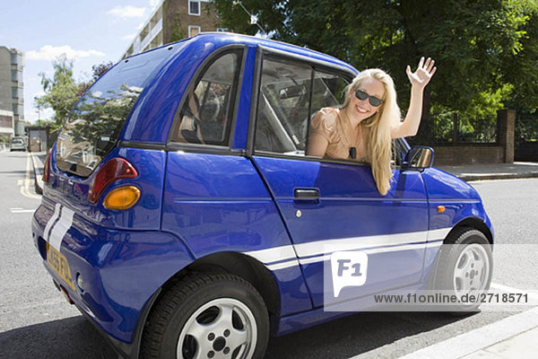 Junge Frau winkt aus dem Elektroauto