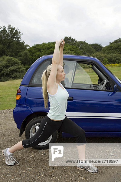 Young woman exercising by electric car