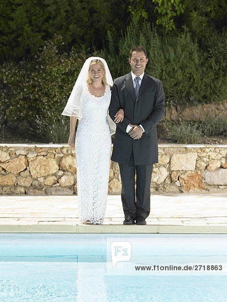 Bride and groom by edge of swimming pool