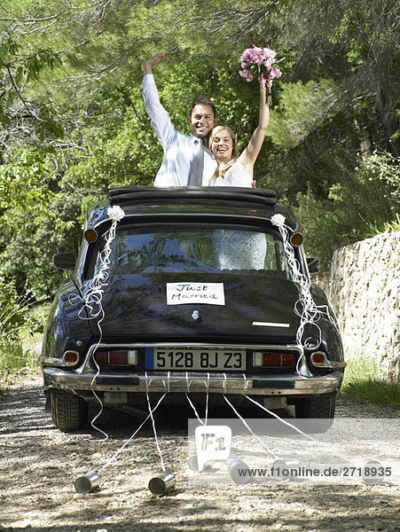 Braut und Bräutigam winken aus dem Hochzeitsauto