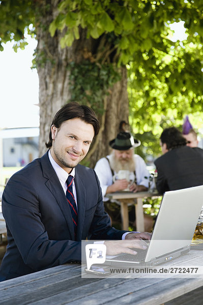 Upper   Young business man in beer garden using laptop  smiling  portrait